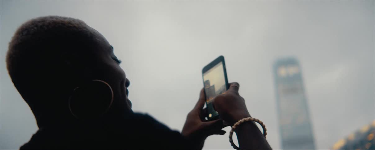Young happy woman filming the city skyline with her smartphone on an overcast day