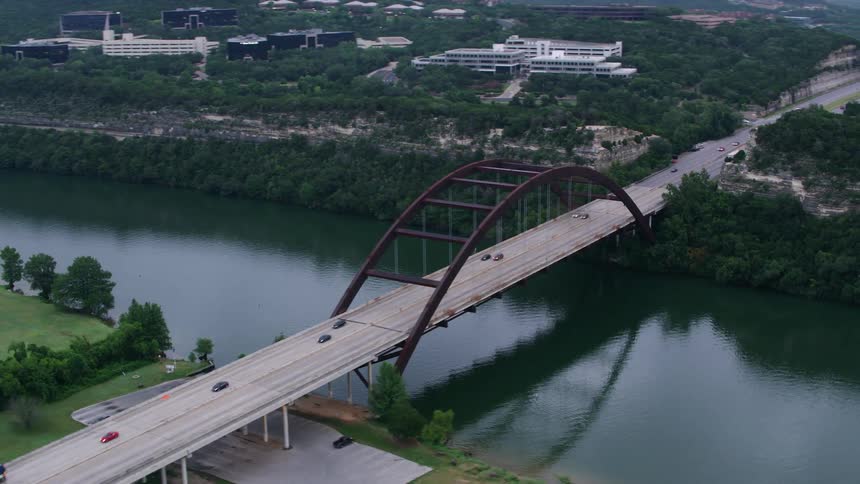 Vehicles cross bridge over river near forest and town