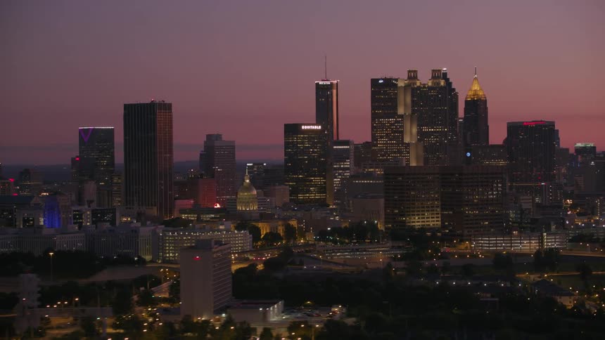 Lights on downtown skyscrapers and buildings glow as the pink sky grows darker