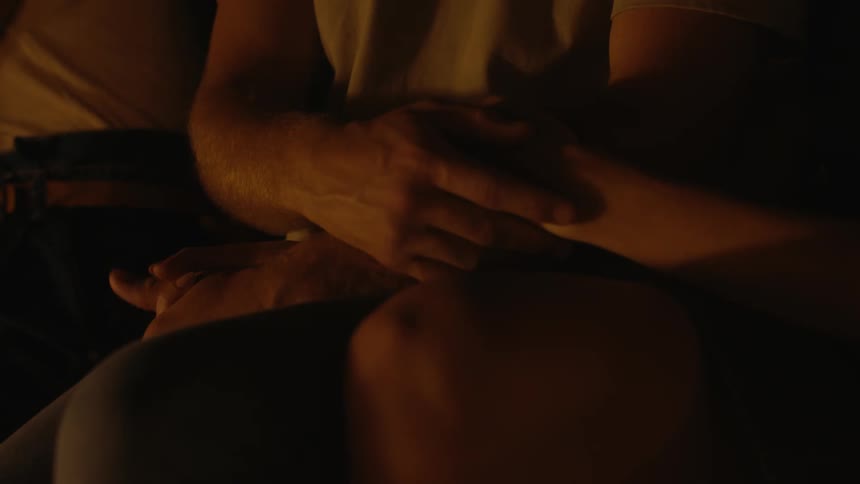 A couple are sitting together in a dark room holding hands