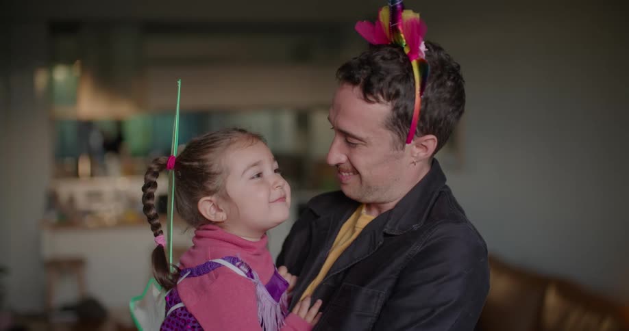A man holds a small girl in his arms while smiling into the camera before turning to talk to the girl
