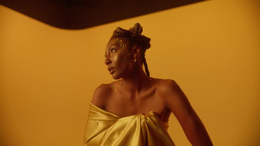 Young beautiful woman wearing golden clothes covered in glitter modeling while standing against a gold background