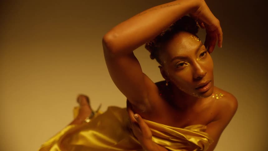 Young beautiful woman wearing golden clothes covered in glitter modeling while sitting on the floor