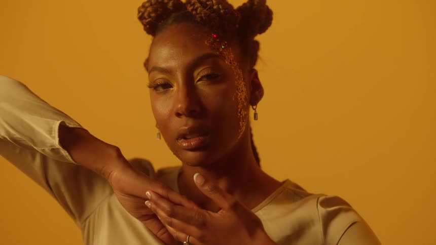 Model with face decorated by glitter moves and poses against studio background
