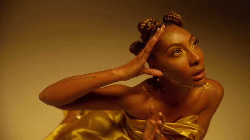 A model covered in glittered and wearing shimmering fabric poses in a studio