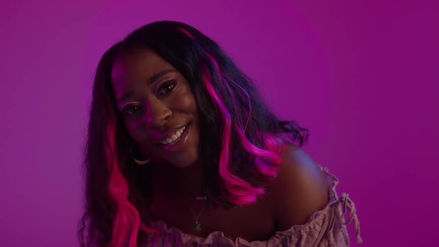 A woman with pink stripes in her hair beckons the camera closer