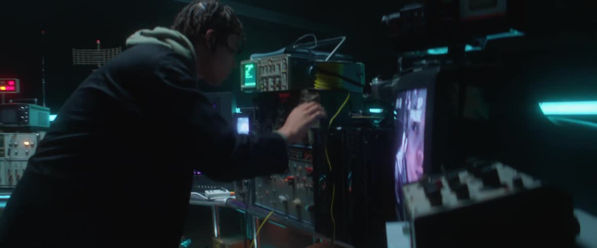 A man is in a room with televisions and monitors hooked up to cameras watching him and he is looking at himself on the screens and turning dials