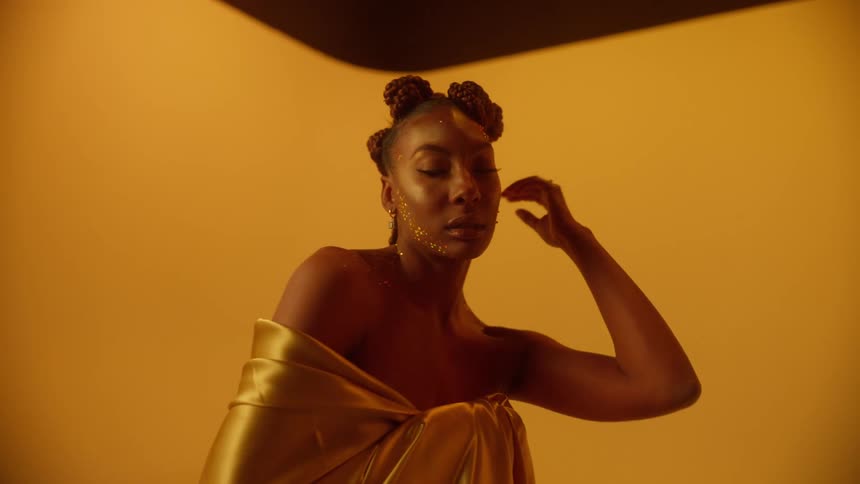 A woman is posing for the camera and wearing a gold dress