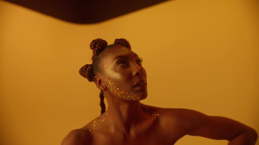 Young beautiful woman wearing golden clothes covered in glitter modeling in front of a yellow background