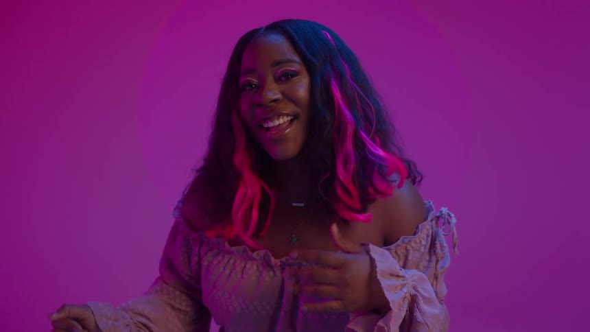Close up of the face of a young woman with colorful makeup and hair dancing in front of a magenta background