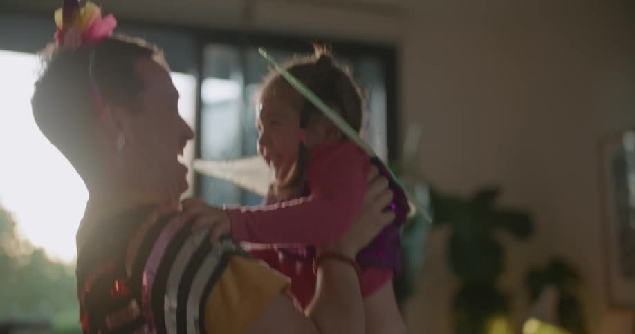A man playfully tosses and catches a small girl in the living room of a house during the day