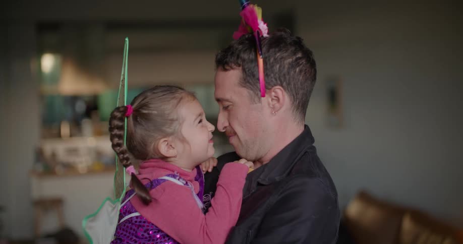 A man wearing a hairband holding and playing with his daughter in fairy wings