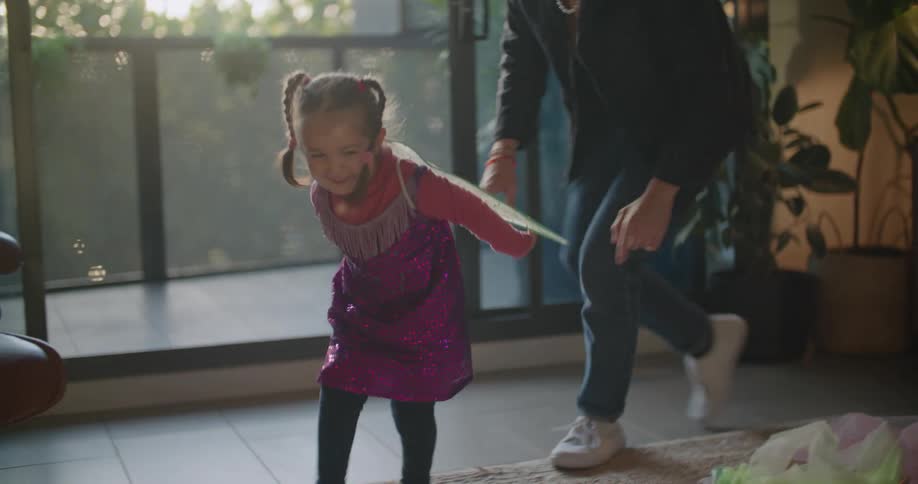 A man chases his daughter around their living room while she wears a butterfly costume