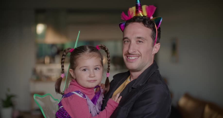 Father and toddler daughter wearing costumes looking at the camera on the living room at morning