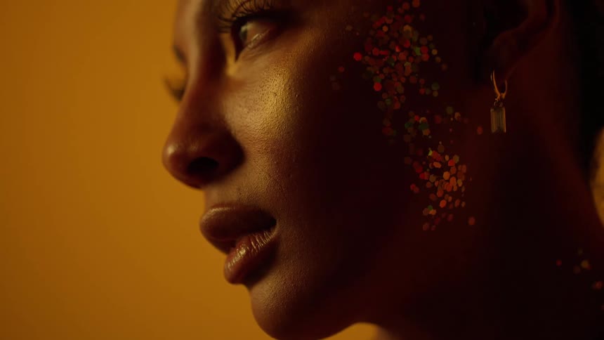 Close up of the face of a beautiful woman covered in glitter in front of a golden background