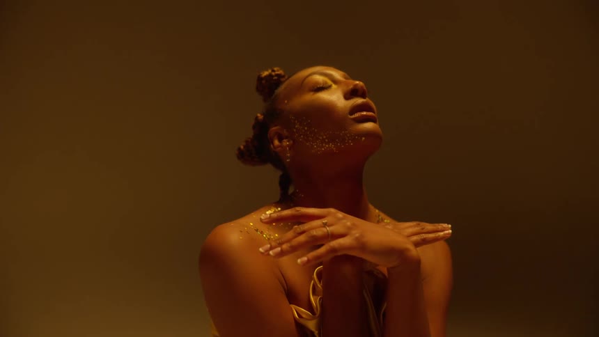Young beautiful woman wearing golden clothes covered in glitter waving her hands while sitting on the floor