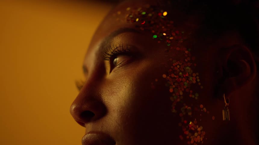 Close up of the face of a beautiful woman covered in glitter in front of a golden background
