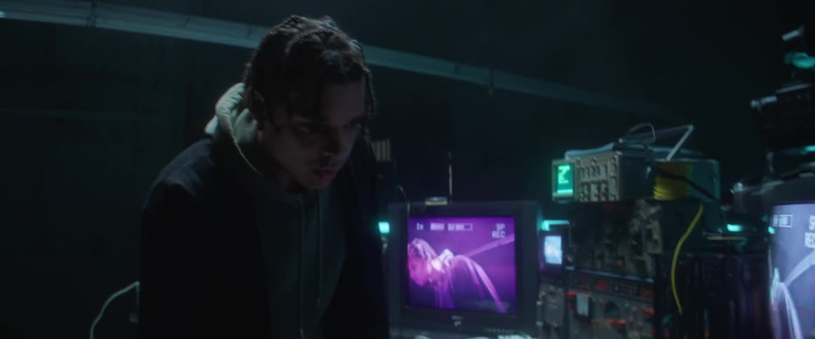 A man is in a room with televisions and monitors hooked up to cameras watching him and he is looking at himself on the screens and turning dials