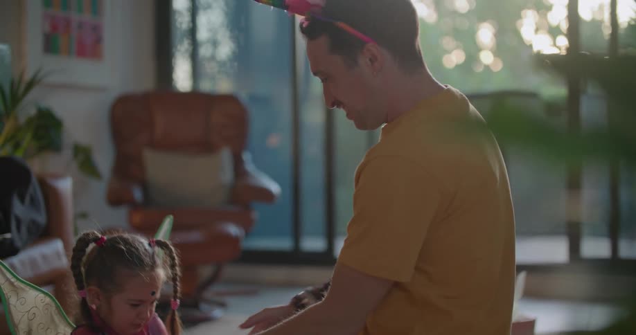 A man is playing with his young daughter who is wearing green fairy wings