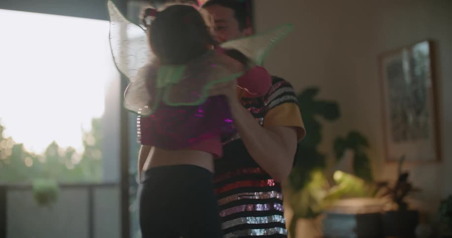 A man spins his daughter around their living room while dressed in a sequined costume