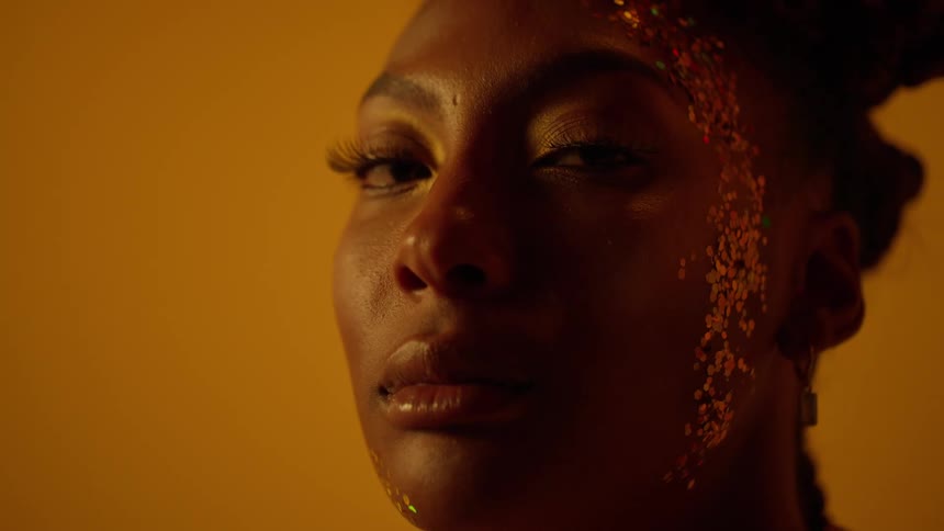 Close up of the face of a beautiful woman covered in glitter in front of a golden background