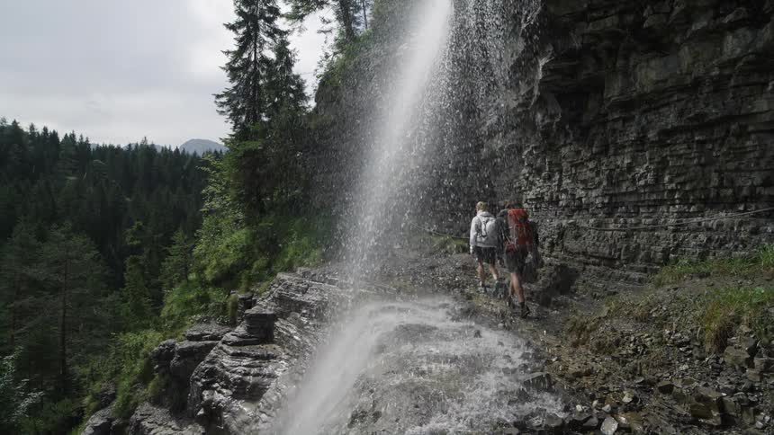 A man and woman hike past a waterfall on a cliff