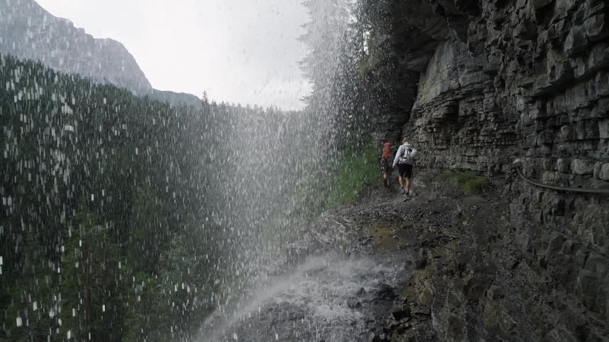 Waterfalls are flowing down the side of a cliff as people are walking on the ledge