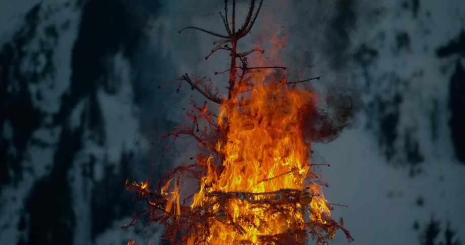 An outside christmas tree is in flames and an ornament hangs from a branch
