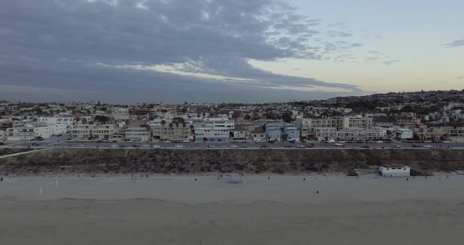 A town is in the distance off the beach with cars driving on a road