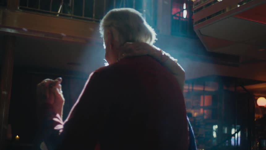 Elderly couple kiss as they dance together in empty room under bright ray of light