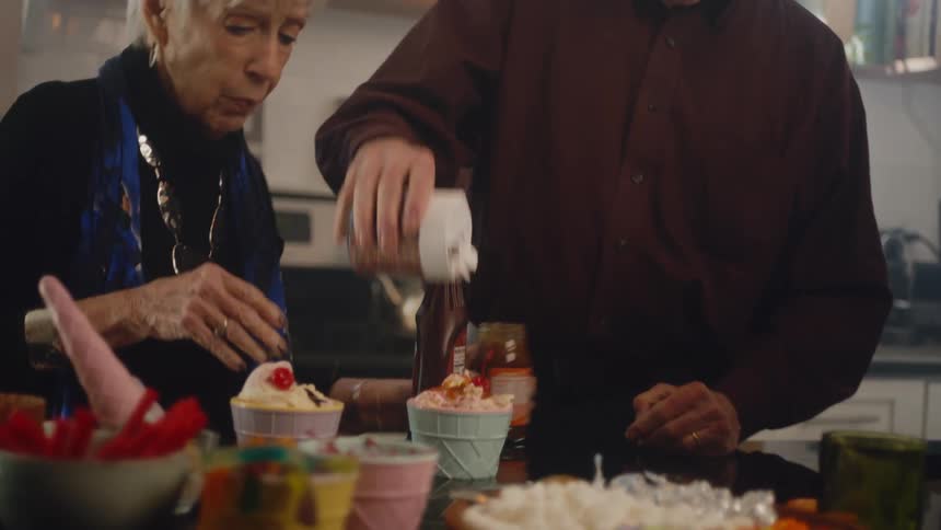 Elderly couple sprinkling toppings on ice cream cups in the kitchen at home