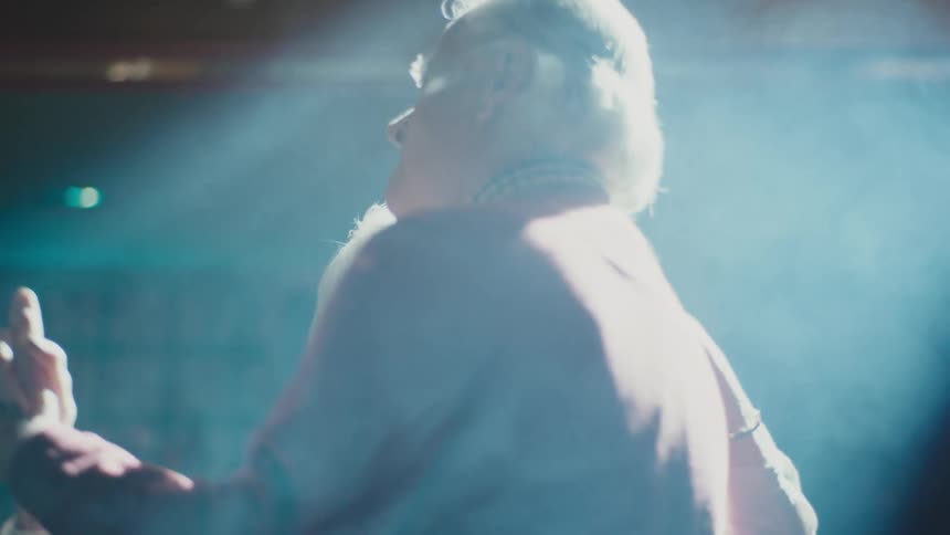 A spotlight shines down on an elderly couple slow dancing smiling and gazing at each other