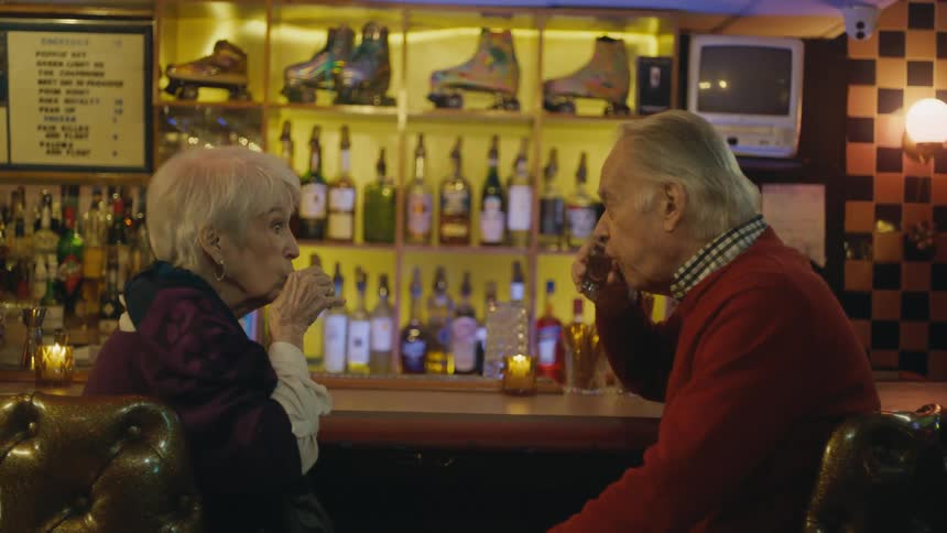 A senior citizen couple are sitting at a bar and doing shots they were served