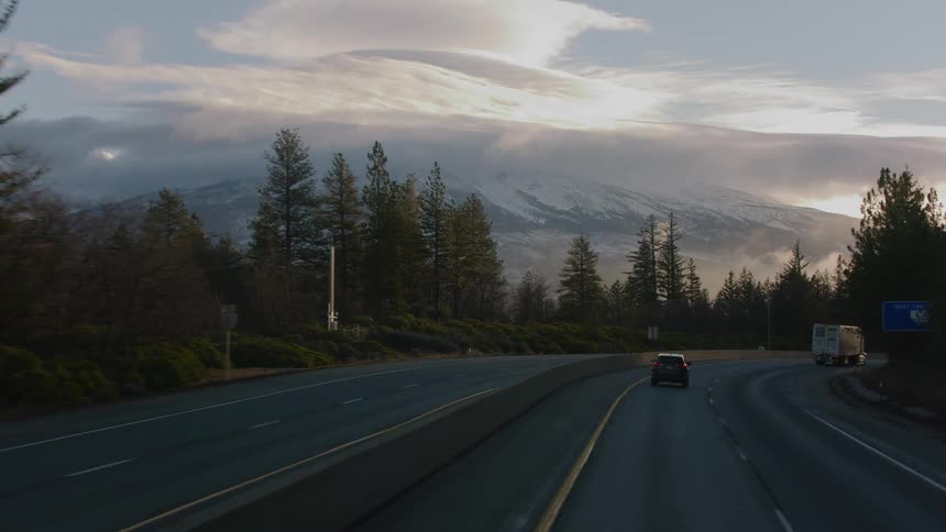 Vehicles driving on a highway through the pine tree forest close to a mountain in the morning