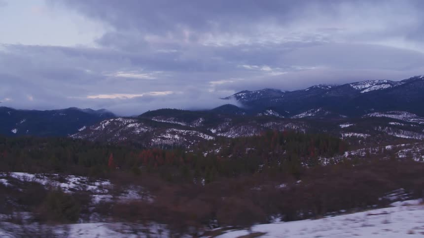 Snow dusted mountain slopes and trees alongside a highway