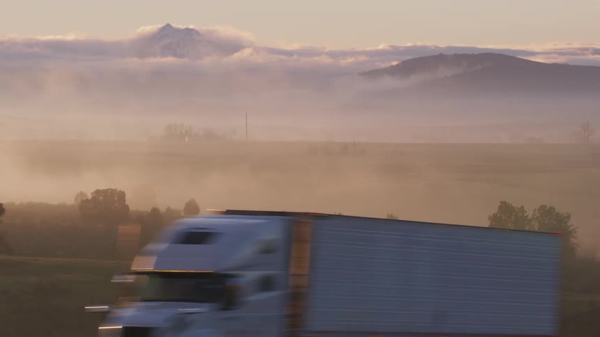 Traveling on a foggy country road with a passing truck and trees and mountains on the horizon high in the clouds