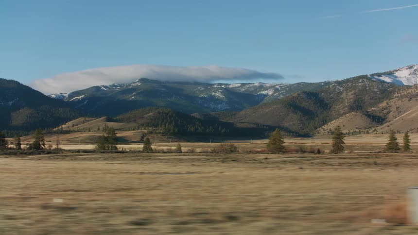Traveling through open land with a few trees and light snow on mountains in the distance