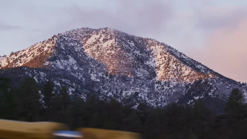 A car is driving by a mountain during the sunset