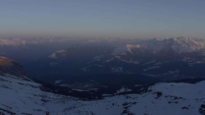 Aerial view of the peaks of a mountain range covered in snow under the mist at morning