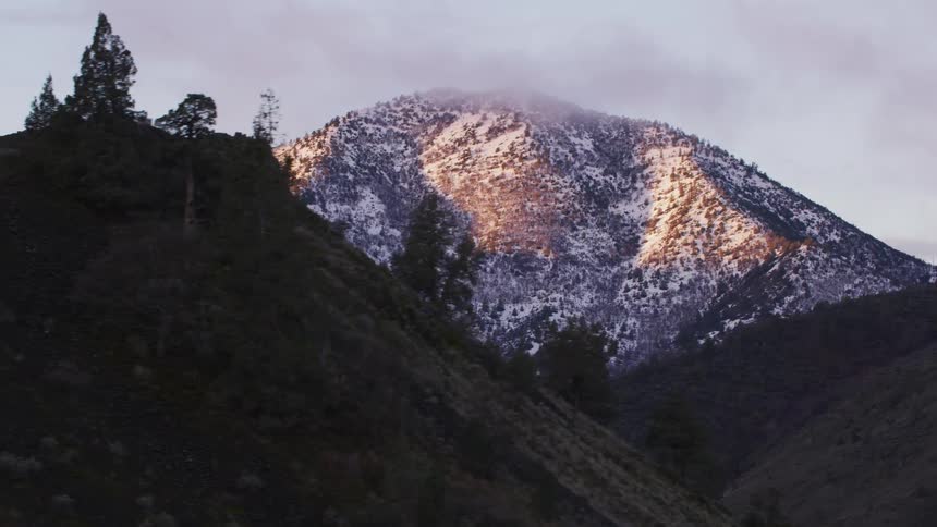 A snow covered mountain looms over a freeway during the day