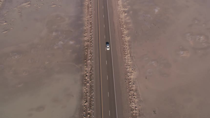 An aerial view of a car driving on a street next to a snowy field