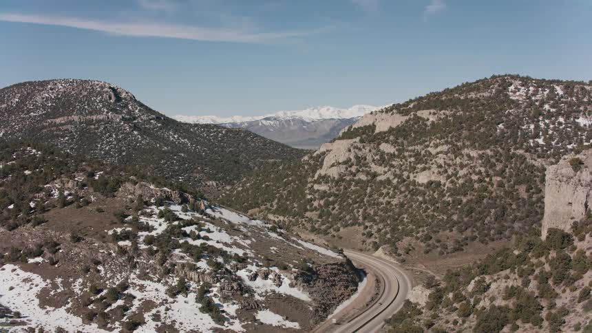 A road winds through mountains and there are snow covered mountains in the distance