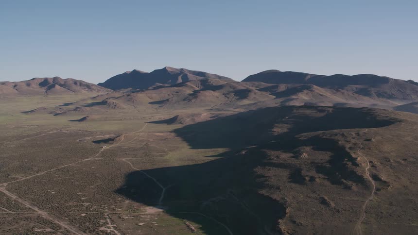 Aerial view of dirt roads stretching across wide open land surrounded by mountains