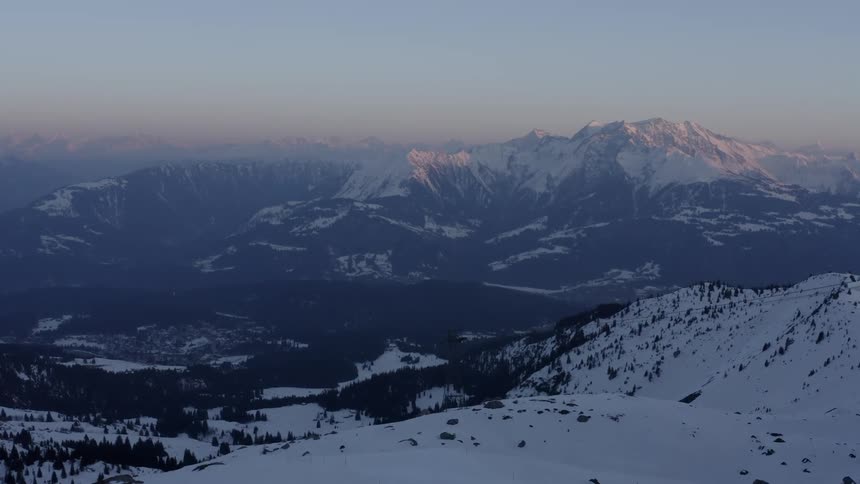 Homes sit on a hill near snow covered mountains