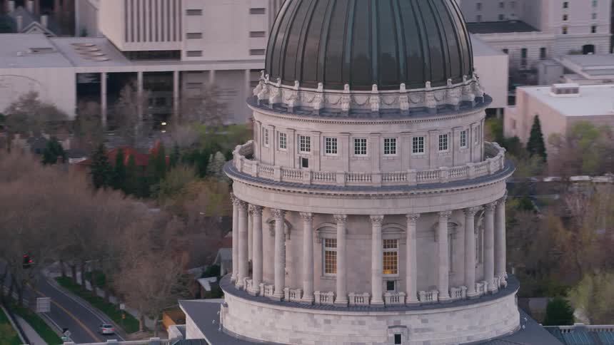 Aerial view of a round domed capitol building and other buildings around it and cars in a parking lot