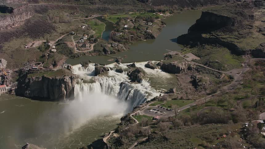 Wide waterfall foams as it flows near small town sitting among uneven terrain near cliffs