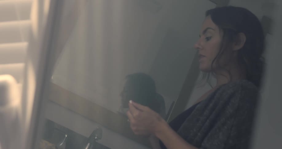 A woman looks at a pregnancy test while standing in a bathroom during the day
