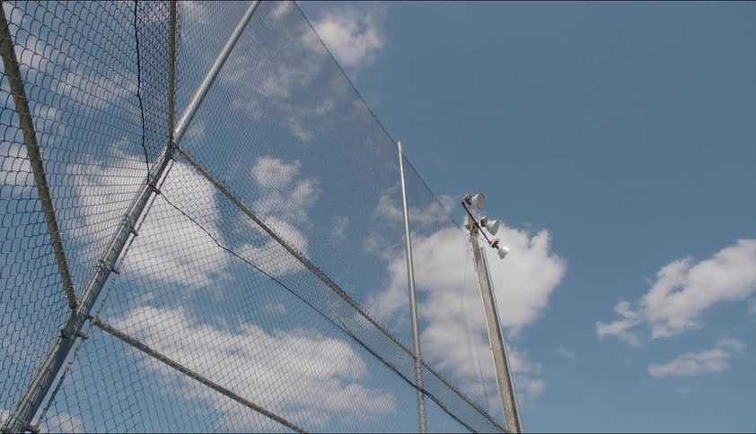 A chain linked fence and light pole reach high in a cloud filled sky