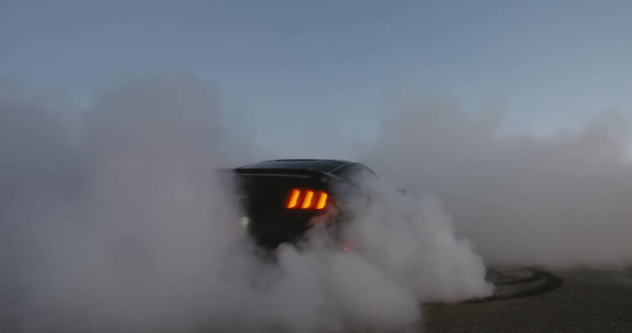 A black sports car turns around in the sand and leaves smoke behind it