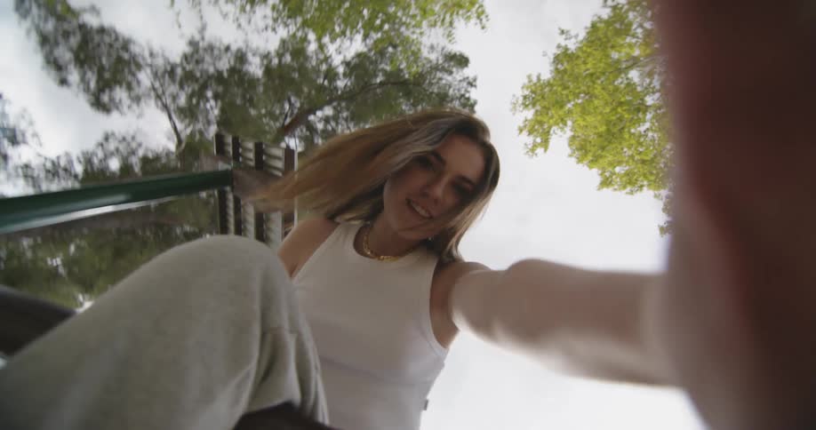 A woman sitting on top of the monkey bars at the playground pushes the camera away laughing